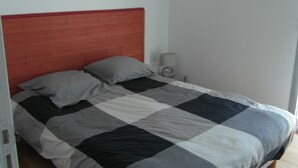 A bedroom with a checkered bedspread, a wooden headboard, and two paintings on the wall. - Appt NEUF (2022) type 2 a 800 mètres ocean (La Rochelle)