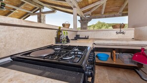 Una cocina con estufa a gas, vigas de techo de madera, chimenea de piedra y vistas al exterior.