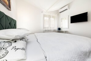 Un dormitorio moderno con un cabecero tapizado en verde, una colcha blanca y un televisor de pantalla plana montado en la pared.
