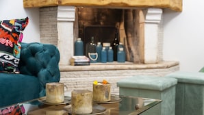 Una sala de estar con un sofá color turquesa, una mesa de centro de vidrio con velas y una chimenea con botellas decorativas.