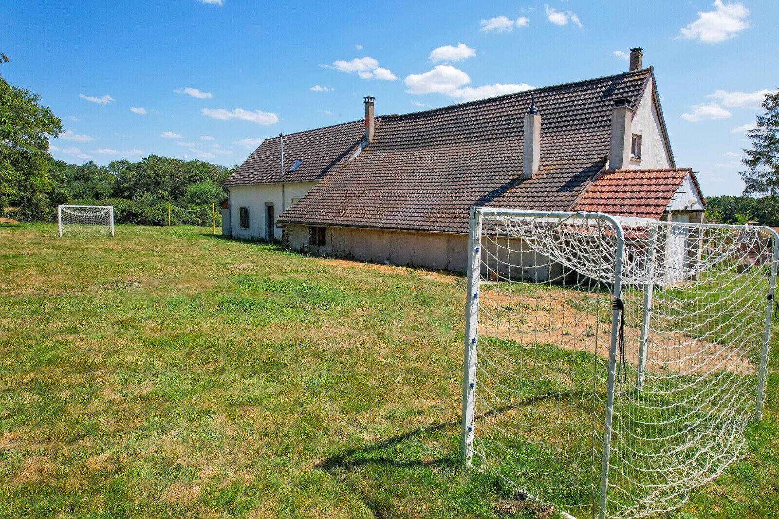 A rural house with a red-tiled roof and a white exterior, surrounded by a grassy field and a soccer goal.