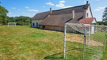 A rural house with a red-tiled roof and a white exterior, surrounded by a grassy field and a soccer goal.