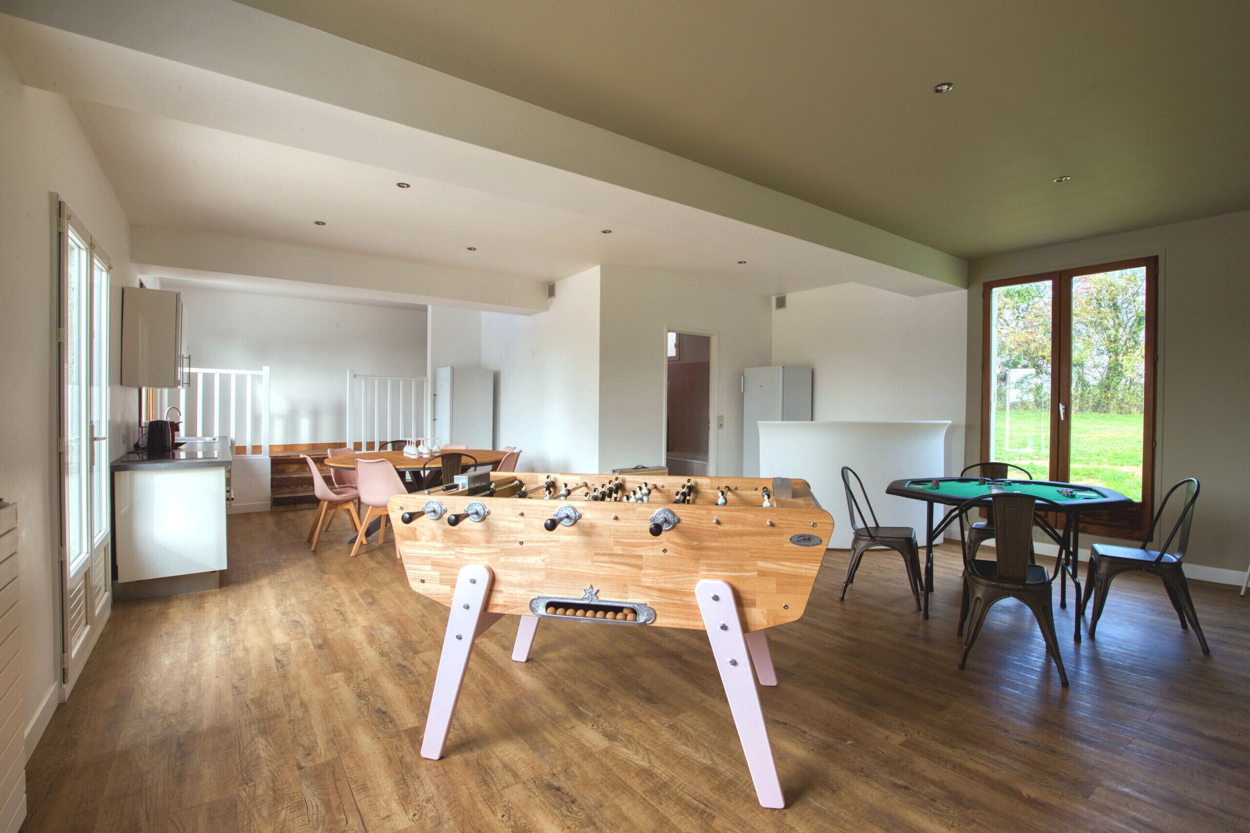 A spacious living area with a wooden foosball table, a pool table, and a dining area with chairs and a table.