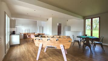 A spacious living area with a wooden foosball table, a pool table, and a dining area with chairs and a table.