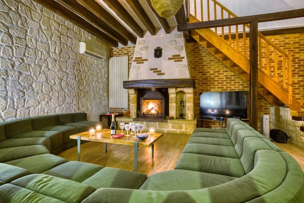 A cozy living room with a stone wall, a fireplace, a wooden staircase, and green upholstered seating.