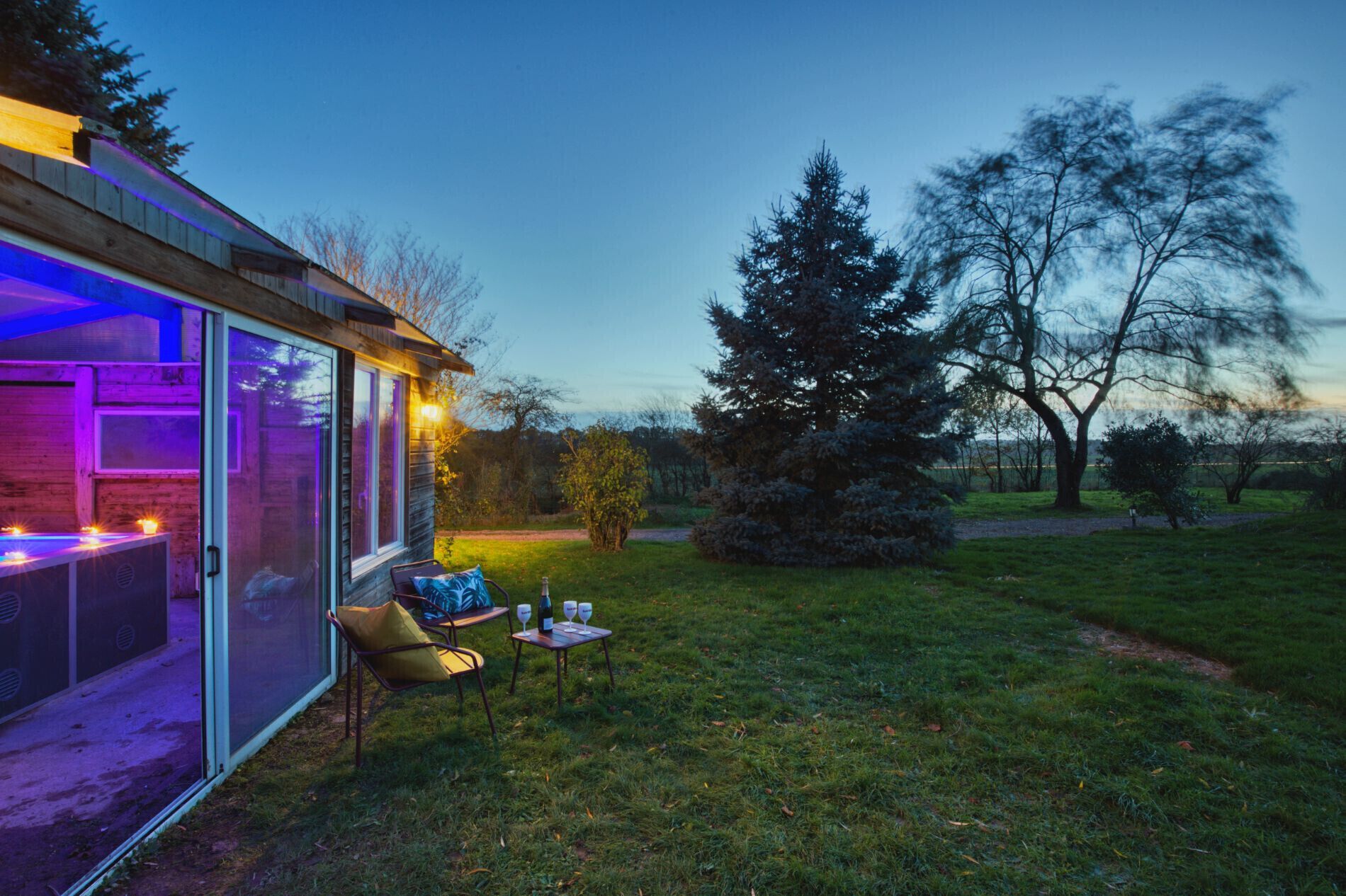 Un área de estar moderna al aire libre con cerramiento de vidrio, una mesa con copas de vino y una silla.