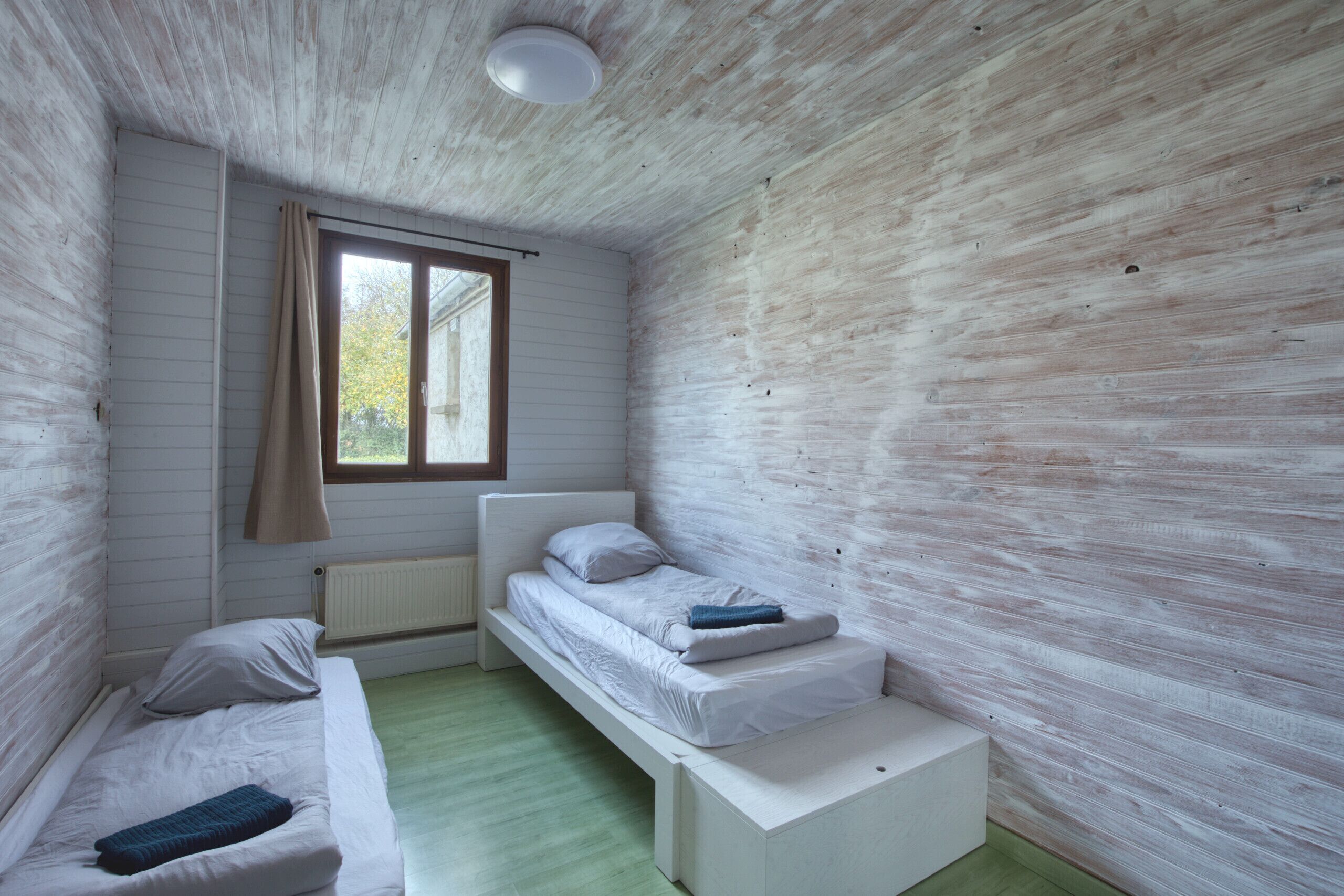 Une petite pièce, de taille modeste, comprenant un lit simple, une fenêtre et un radiateur.