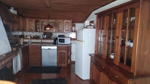 A kitchen with wooden cabinets, a white refrigerator, a microwave, and a dishwasher. - ABRIGO DO CABECINHO (Cortes do Meio)