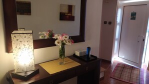 A hotel reception area with a reception desk, a large mirror, a vase with flowers, a standing lamp, and a door with a sign. - ABRIGO DO CABECINHO (Cortes do Meio)