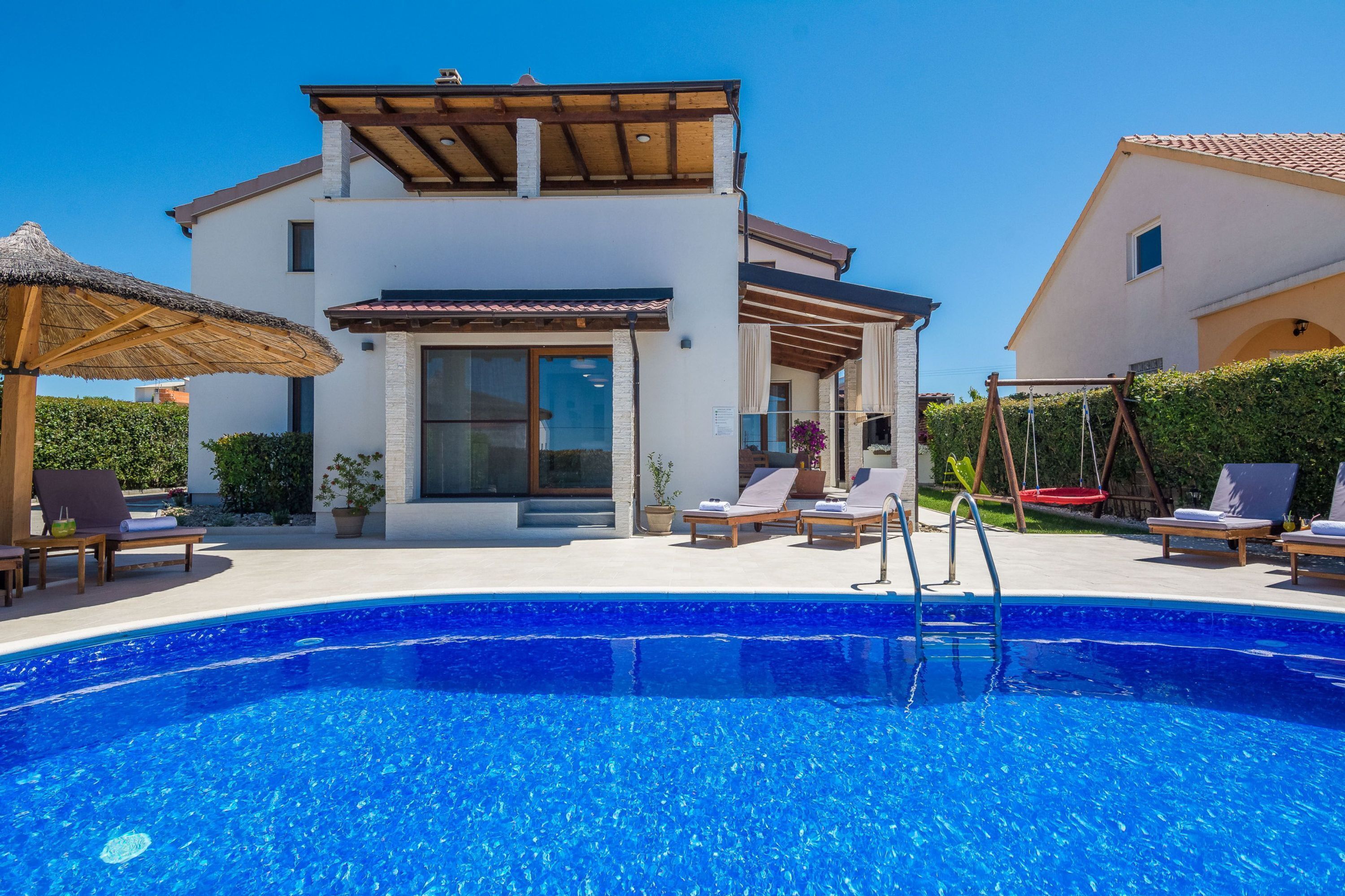 A modern house with a swimming pool, lounge chairs, and a pergola.
