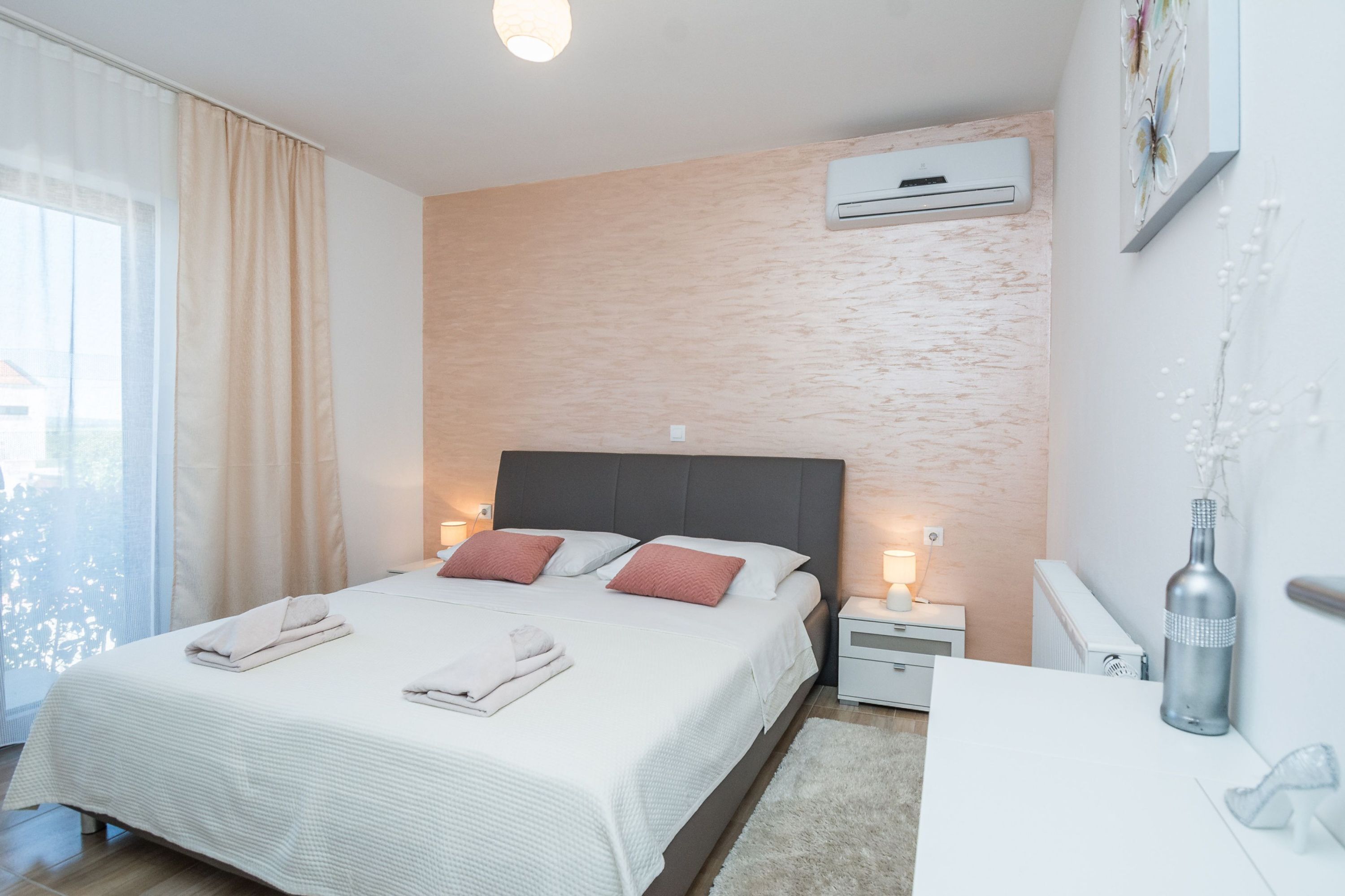 A neatly arranged bedroom with a bed, bedside tables, an air conditioning unit, and a bottle on the nightstand.