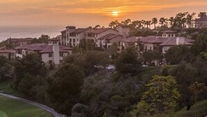 Un complejo turístico frente al mar con varias villas, un campo de golf y vistas al océano al atardecer.