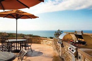 An outdoor patio with a stone wall, a grill, and a table with chairs. - Marriott's Newport Coast Villas 2 Bedroom 2 Bath (Newport Beach)