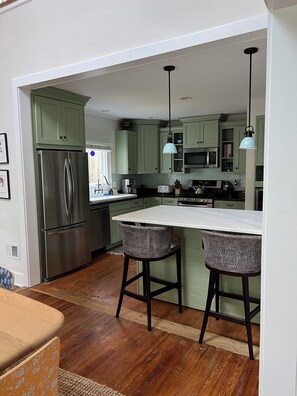 Una cocina moderna con armarios verdes, electrodomésticos de acero inoxidable y una isla central con taburetes de bar.