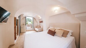 Ein Schlafzimmer mit einem großen Bett, einer kleinen Sitzecke und Blick ins Freie durch eine Glastür.