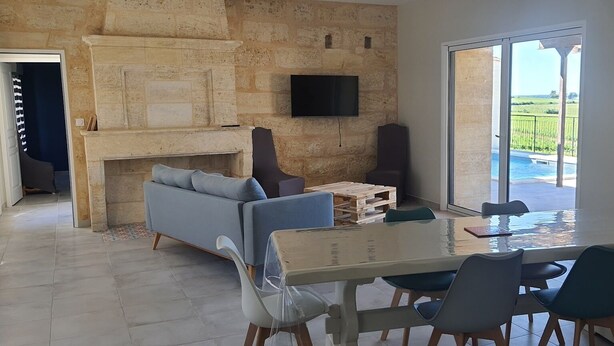 A modern living room with a stone fireplace, a sofa, a TV mounted on the wall, and a dining area with a table and chairs.