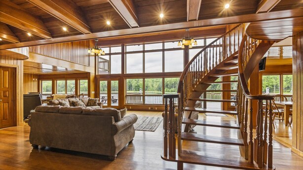 A spacious living room with a large wooden staircase, a sofa, and large windows offering a view of the outdoors. - Custom built resort on private lake with kayaks, hiking, (Little Meadows)