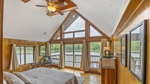 A bedroom with a large bed, wooden walls, a ceiling fan, and large windows overlooking a lake. - Custom built resort on private lake with kayaks, hiking, (Little Meadows)