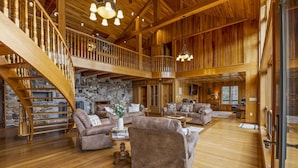 A spacious living area with a wooden staircase, leather sofas, and a stone fireplace. - Custom built resort on private lake with kayaks, hiking, (Little Meadows)