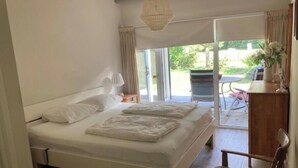 Un dormitorio con una cama grande, una mesita de noche con lámpara, una silla y vistas a un patio exterior.