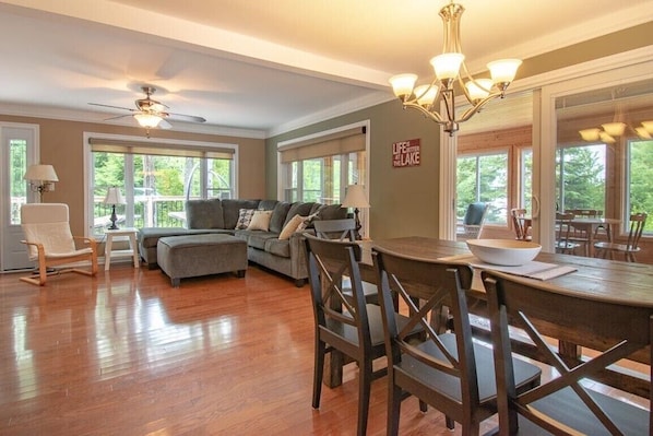 A spacious living room with a large sofa, a dining table with chairs, and a ceiling fan.