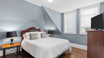 A bedroom with a large bed, two bedside tables with lamps, a wooden headboard, and a TV on a cabinet.