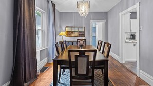 A dining room with a wooden table, chairs, a chandelier, and a painting on the wall. - Historic 1908 Frenchtown Home (Saint Charles)