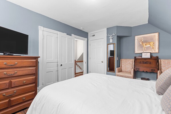 A bedroom with a large bed, a dresser, a television, and a deer wall art piece.