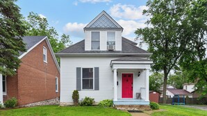 A two-story house with a red door, white siding, and a small front porch. - Historic 1908 Frenchtown Home (Saint Charles)