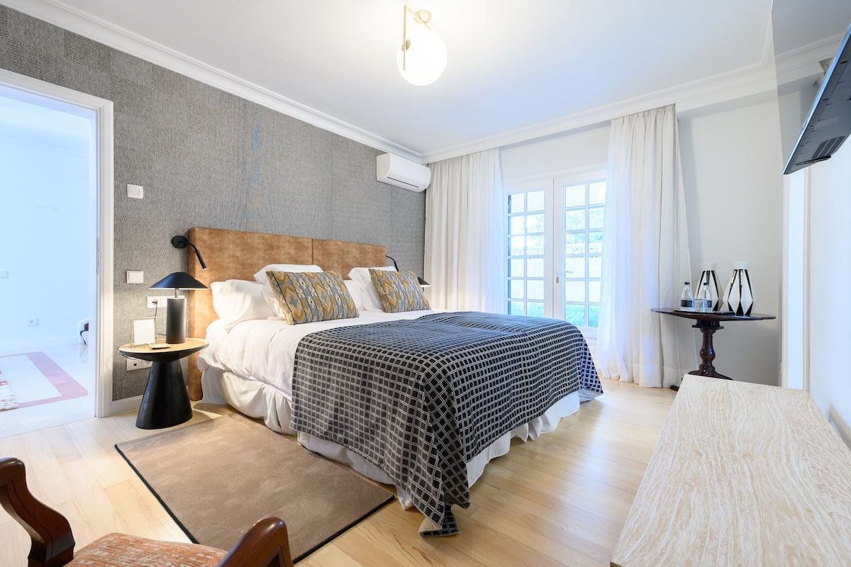 Ein modernes Schlafzimmer mit einem großen Bett, Nachttischen, einem Schreibtisch und einem Fenster mit Vorhängen.