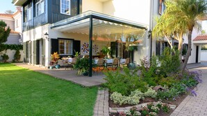 A two-story house with a covered patio, a well-maintained garden, and a clear sky.