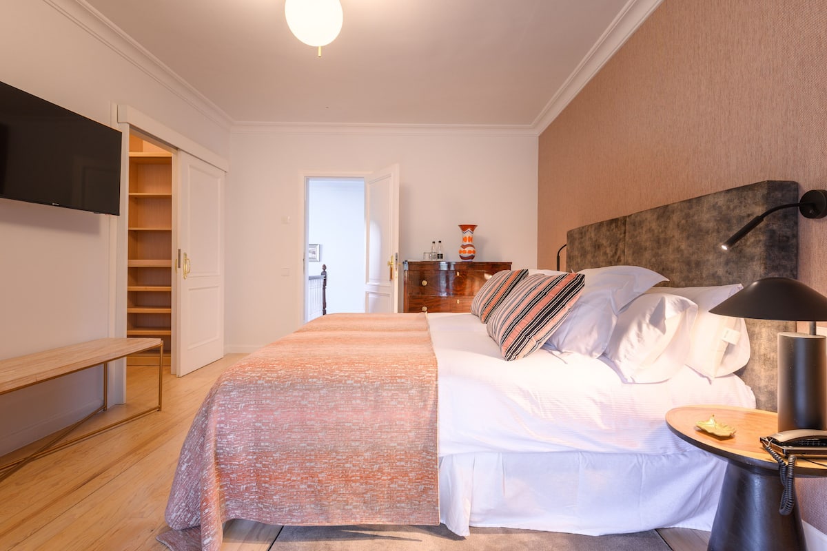 Ein Hotelzimmer mit Bett, Nachttisch, Lampe und einem an der Wand befestigten Fernseher.