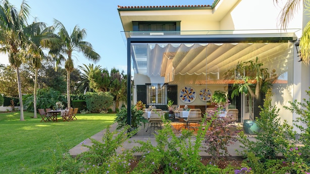 A modern house with a covered patio, outdoor dining area, and lush garden.