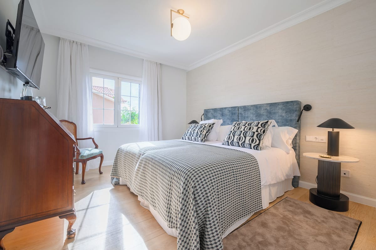 Ein Schlafzimmer mit Bett, Schreibtisch, Stuhl, Lampe und Fenster.