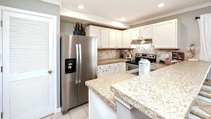 Una cocina moderna con armarios blancos, un refrigerador de acero inoxidable y una encimera de granito.