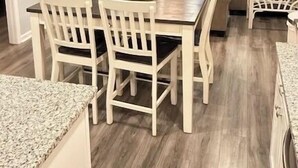 Un coin repas avec une table et des chaises en bois, un ventilateur de plafond et une vue sur l’océan grâce à de grandes fenêtres.