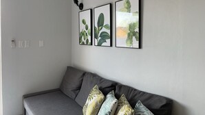 Ett modernt vardagsrum med en grå soffa, tre inramade botaniska tryck på väggen och en svart vägglampa.