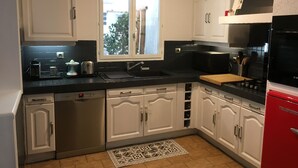 Una cocina con armarios blancos, encimera negra, una ventana y un refrigerador rojo.