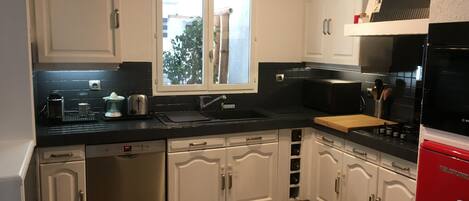 A kitchen with white cabinets, a black countertop, a window, and a red refrigerator.