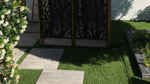 Un jardín con una cerca decorativa, un pequeño banco de madera y un sendero.