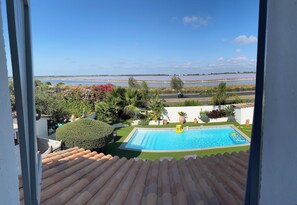 A view from a balcony overlooking a swimming pool with a clear blue sky and a distant body of water.