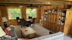 A cozy living room with a plaid sofa, a coffee table, and a bookshelf filled with books. - Heros Hideaway, private 1acre flat grassy yard, majestic sunsets (South Hero)