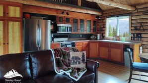 Ein gemütliches Blockhaus-Interieur mit Küche, Essbereich und Wohnzimmer, das eine Ledersofa beherbergt.