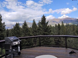 Une terrasse en bois avec un barbecue, offrant une vue sur une chaîne de montagnes boisées.