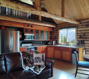 Un intérieur de chalet chaleureux comprenant une cuisine, un coin repas et un salon avec un canapé en cuir.