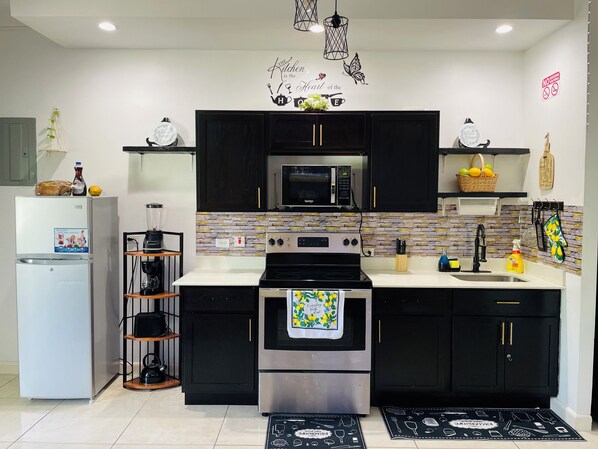 A modern kitchen with black cabinets, a stainless steel stove, a microwave, and a refrigerator. - Chic Modern Retreat (Kingston 19)