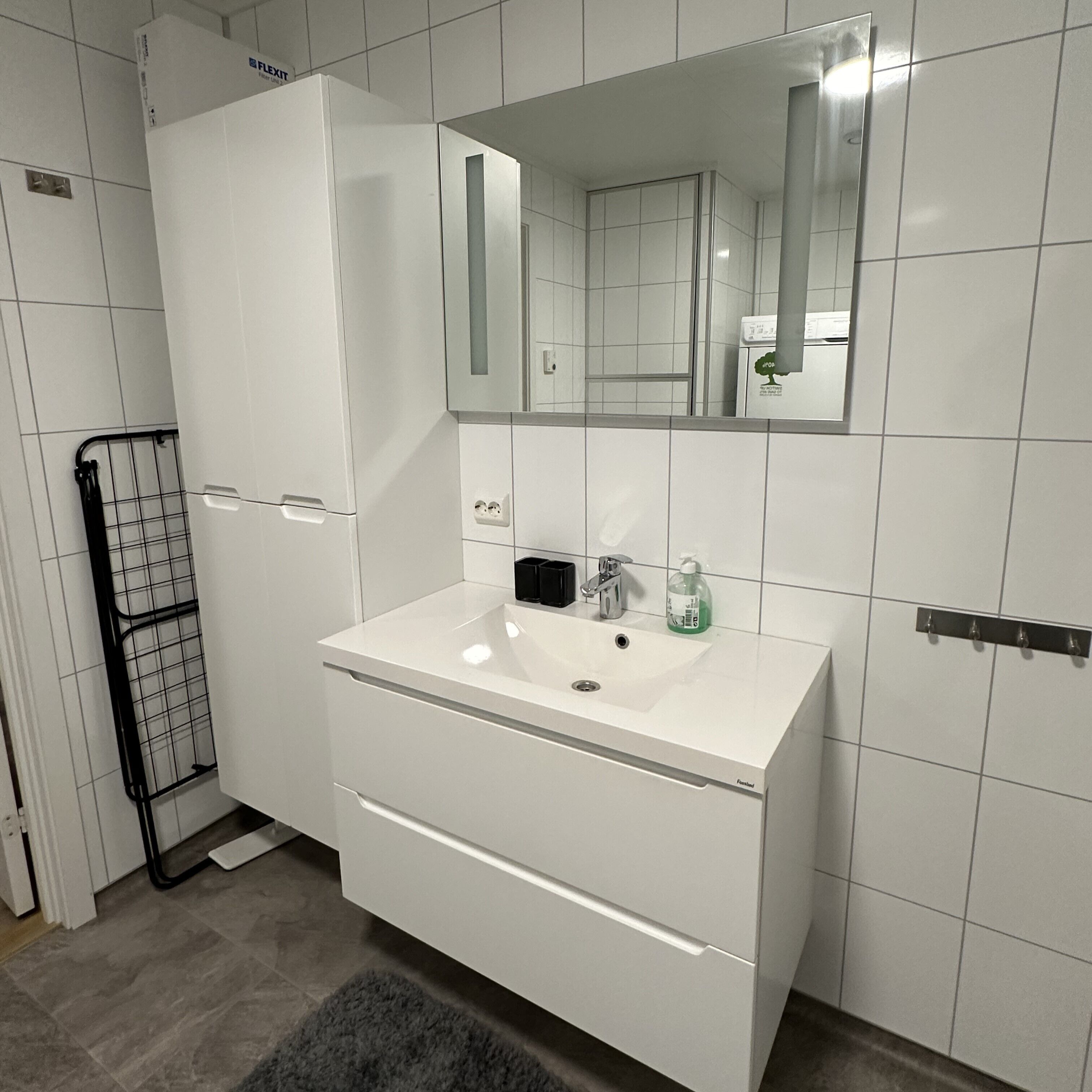 A modern bathroom with a white sink, mirror, and a towel rack.