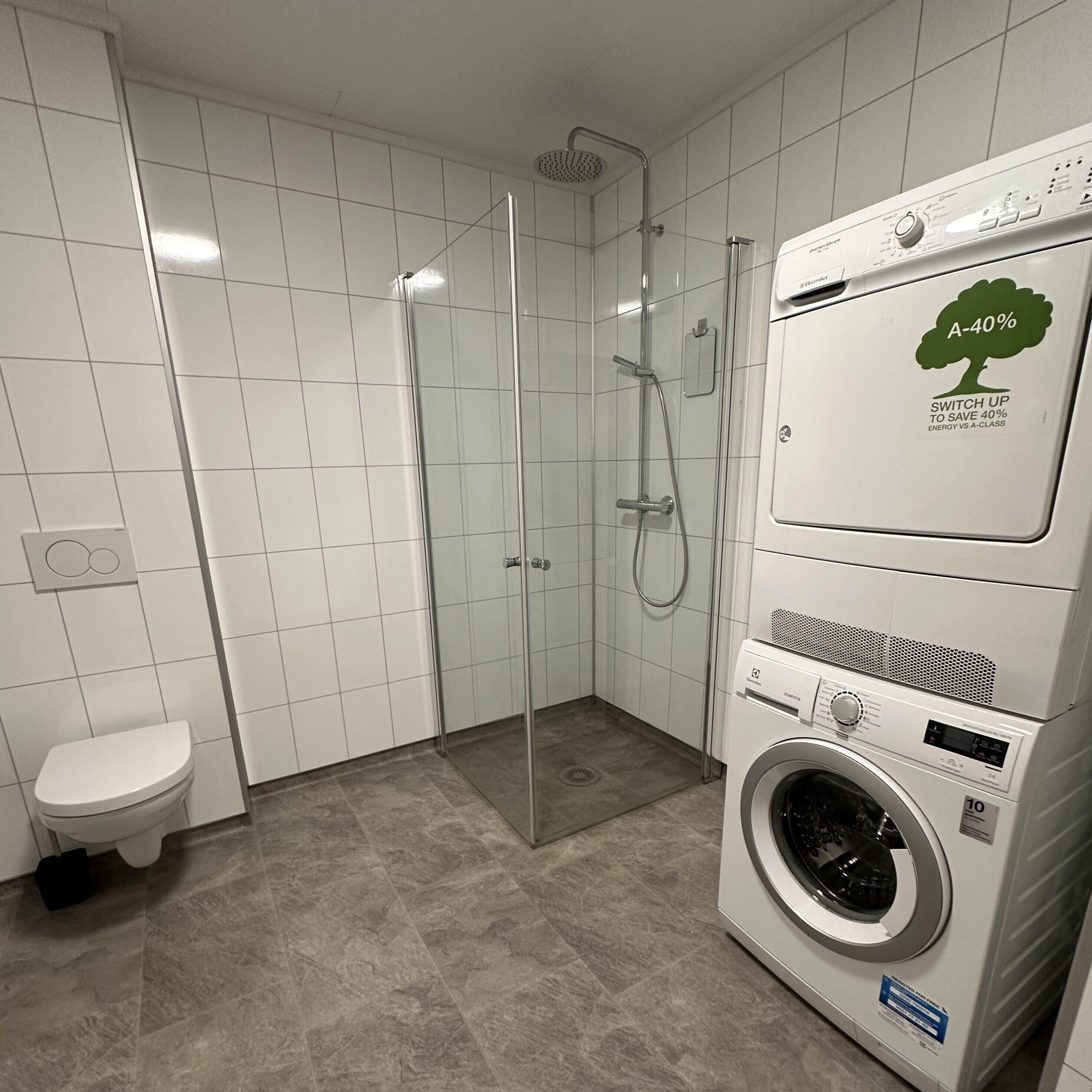 Een moderne badkamer met een douchecabine, een toilet en een wasmachine en droger boven elkaar.
