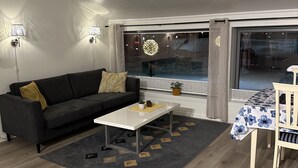 A modern living room with a sofa, coffee table, and a dining area with a table and chairs. - Lofoten Overnatting - Leknes - Hostel (Vestvågøy)