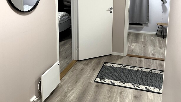 A room with a wooden floor, a white door, a mirror, and a small rug. - Lofoten Overnatting - Leknes - Hostel (Vestvågøy)